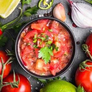 A bowl of salsa surrounding by ingredients.